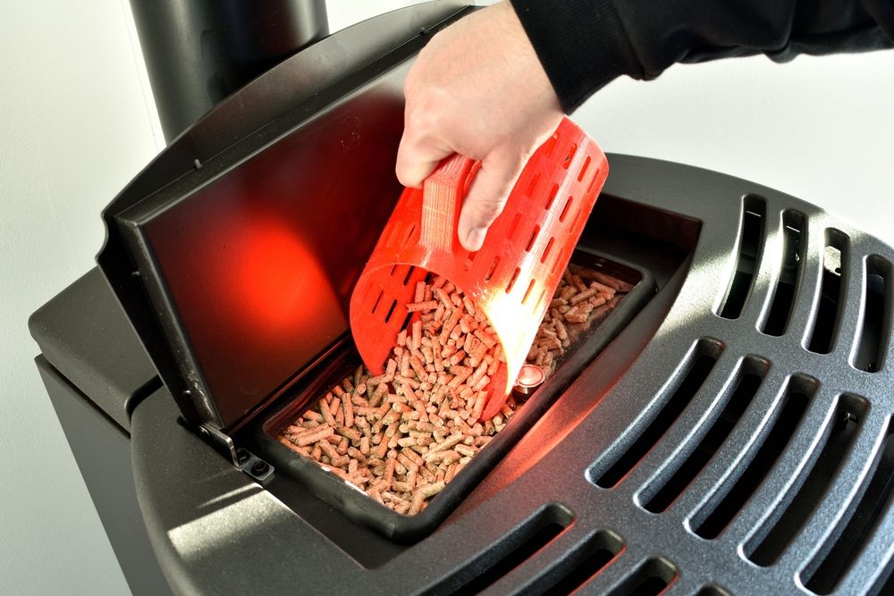 A close up of a wood pellet stove with a person placing the pellets inside