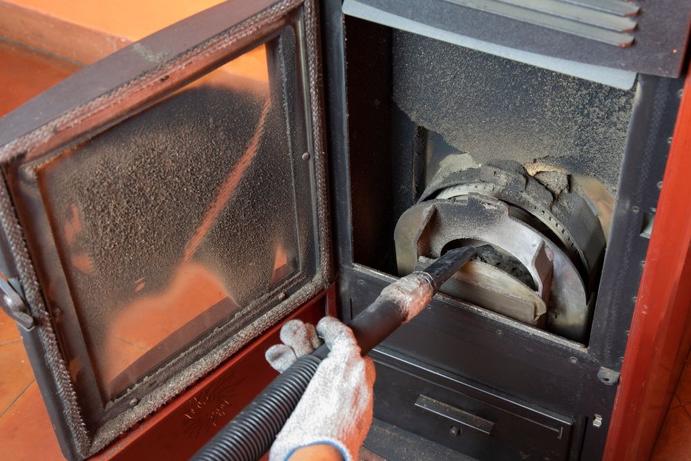 A worker cleans the inside of a pellet stove with a vaccum tube